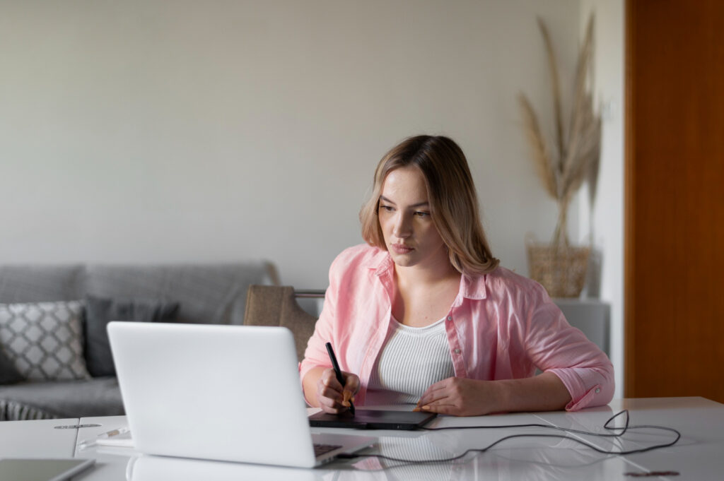 Imagem ilustrativa: jovem de camisa rosa estuda em frente ao notebook com caneta e mesa digitalizadora, cena que remete ao curso de Auxiliar de Saúde Bucal