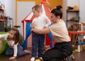 Profissional acompanhando duas crianças pequenas durante brincadeira em sala de creche