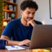 Jovem brasileiro estudando pelo notebook com materiais de apoio, representando cursos de qualificação profissional.