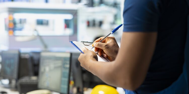 Pessoa escreve em bloco de notas segurando óculos, com capacete amarelo e monitores ao fundo, simbolizando os cursos técnicos que abrem portas.