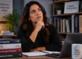 Estudante de língua portuguesa em ambiente de estudo, refletindo enquanto consulta materiais de gramática e escrita em uma mesa com livros.