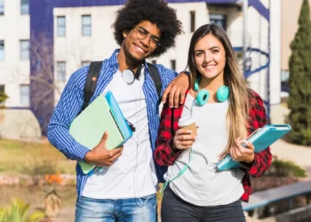 Dois estudantes com livros em frente a uma universidade representam graduações apontadas como algumas das mais valiosas do mercado.