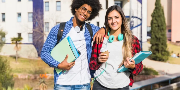 Dois estudantes com livros em frente a uma universidade representam graduações apontadas como algumas das mais valiosas do mercado.