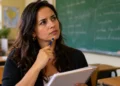 Mulher com caderno em sala de aula, com expressão pensativa, representando a dúvida sobre o uso de “amnésia” ou “aminésia”.