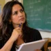 Mulher com caderno em sala de aula, com expressão pensativa, representando a dúvida sobre o uso de “amnésia” ou “aminésia”.