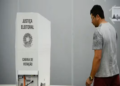 Homem adulto caminha até cabine de votação da Justiça Eleitoral do Brasil em ambiente interno, simbolizando a folga relacionada às eleições.