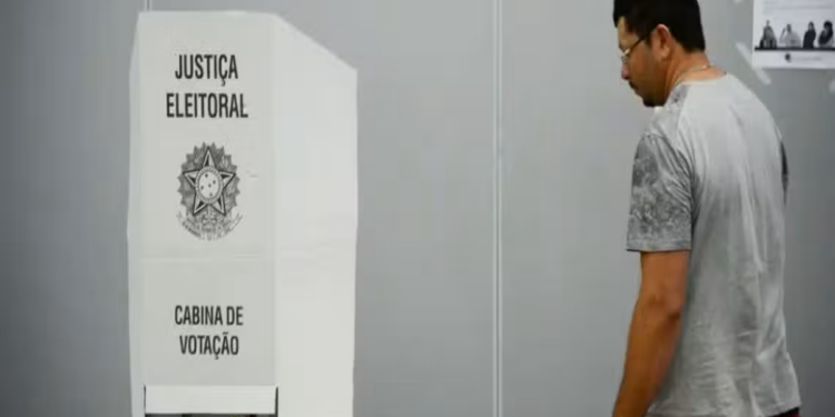 Homem adulto caminha até cabine de votação da Justiça Eleitoral do Brasil em ambiente interno, simbolizando a folga relacionada às eleições.