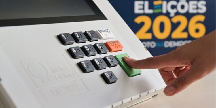 Dedo pressionando a tecla "confirma" de uma urna eletrônica, com o painel numérico em destaque e a marca Eleições 2026 ao fundo.