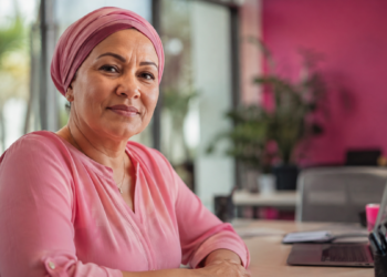 Mulher com lenço rosa em ambiente de trabalho representa reinserção profissional após câncer de mama.
