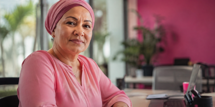 Mulher com lenço rosa em ambiente de trabalho representa reinserção profissional após câncer de mama.