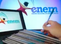 Logo do Enem exibido em telas de computador enquanto uma pessoa faz anotações em caderno de estudos.