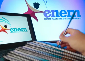 Logo do Enem exibido em telas de computador enquanto uma pessoa faz anotações em caderno de estudos.