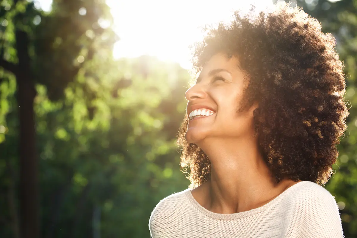 Mulher sorrindo ao ar livre representa força mental e equilíbrio emocional.