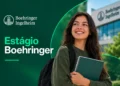 Jovem mulher com caderno e mochila sorri em frente ao prédio da Boehringer Ingelheim, simbolizando as inscrições para o programa de estágio 2027.