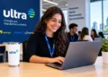 Jovem mulher sorrindo digita no notebook com crachá Ultra em escritório moderno, simbolizando o estágio da Ultrapar.