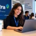 Jovem mulher sorrindo digita no notebook com crachá Ultra em escritório moderno, simbolizando o estágio da Ultrapar.