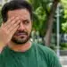 Homem cobre um dos olhos com a mão em uma praça, representando a expressão “fazer vista grossa”.