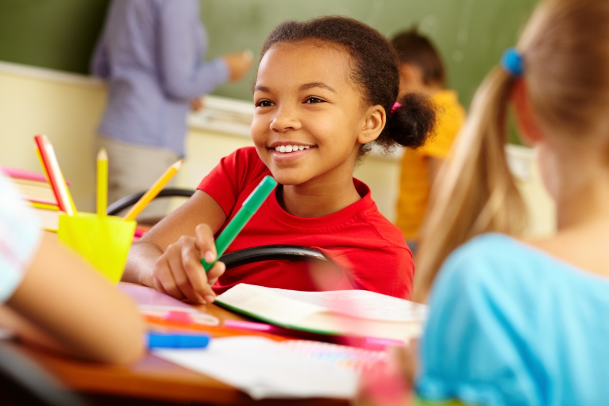 Imagem ilustrativa de estudante sorridente em sala de aula, com caderno aberto e material escolar sobre a carteira, representando o cumprimento dos dias letivos no calendário de 2027.