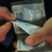 Mãos contando cédulas de cem reais, representando o valor liberado no saque do FGTS aos trabalhadores que cumprem os critérios.