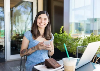 Mulher com celular ao lado de notebook representa acesso ao Fies Empreendedor para contratação de crédito.