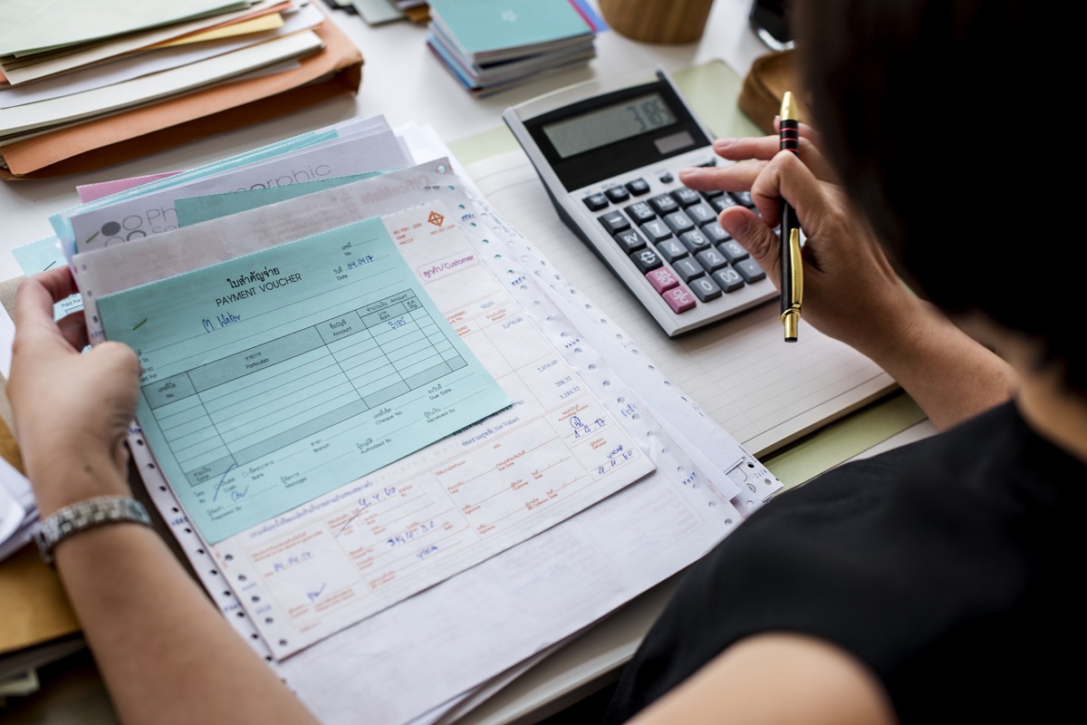 Pessoa usando calculadora e conferindo comprovantes de pagamento azuis e papéis em mesa de escritório, simbolizando o prazo de adequação, caso o adicional de 40% seja aprovado.