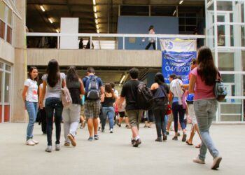 Imagem ilustrativa de jovens com mochilas caminhando pelo saguão de um prédio universitário, em referência ao formato da primeira fase da Fuvest 2027
