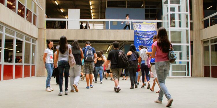 Imagem ilustrativa de jovens com mochilas caminhando pelo saguão de um prédio universitário, em referência ao formato da primeira fase da Fuvest 2027