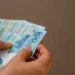 Mãos segurando notas de dinheiro em referência às formas flexíveis de gerar renda para estudantes em 2026.