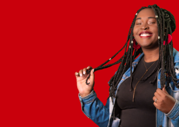 Jovem sorridente de jaqueta jeans posando sobre fundo vermelho, na identidade visual usada na divulgação do programa jovem aprendiz do iFood.