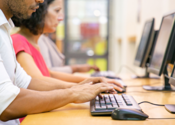 Profissionais utilizam computadores em ambiente de trabalho para realizar tarefas de informática.