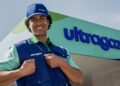 Colaborador sorridente com boné e colete da Ultragaz em frente a uma unidade da empresa, com o letreiro da marca ao fundo.