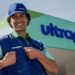 Colaborador sorridente com boné e colete da Ultragaz em frente a uma unidade da empresa, com o letreiro da marca ao fundo.