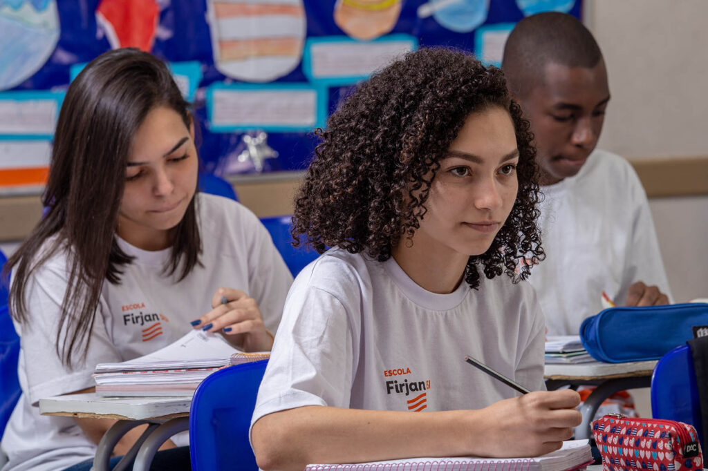 Imagem ilustrativa: estudantes com camisetas da Firjan fazem anotações em sala, cena ligada a cursos técnicos gratuitos
