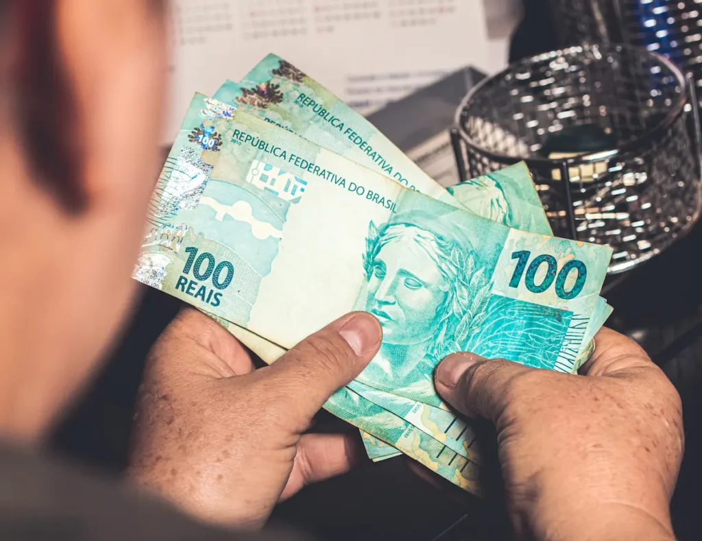 Pessoa segura cédulas de R$ 100, representando a remuneração paga aos participantes do Programa Aprendiz BB.
