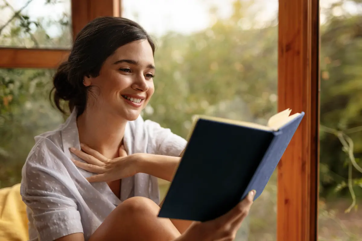 Mulher lendo um livro em ambiente iluminado, representando os benefícios da leitura para o desenvolvimento intelectual.