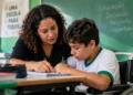 Professora auxilia estudante com deficiência em atividade escolar inclusiva em sala de aula