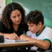 Professora auxilia estudante com deficiência em atividade escolar inclusiva em sala de aula
