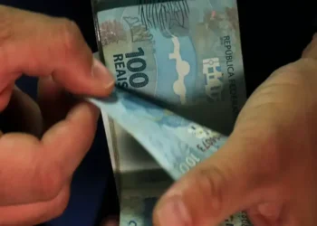 Mãos masculinas contam várias cédulas de 100 reais do Brasil, simbolizando os pagamentos do INSS de setembro.