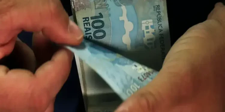 Mãos masculinas contam várias cédulas de 100 reais do Brasil, simbolizando os pagamentos do INSS de setembro.