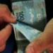 Mãos masculinas contam várias cédulas de 100 reais do Brasil, simbolizando os pagamentos do INSS de setembro.
