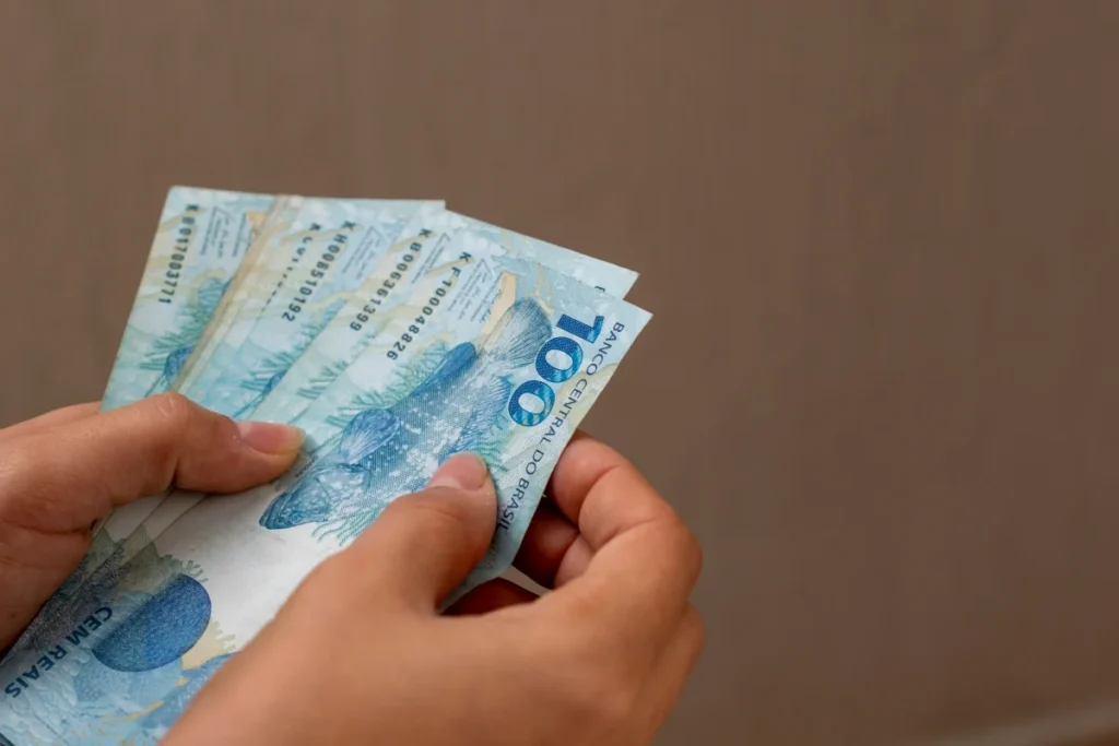 Mãos segurando cédulas de real brasileiro representando o pagamento do 13º salário CLT em 2026