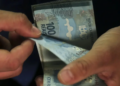 Mãos contando cédulas de cem reais, tema do pagamento do INSS de setembro de 2026