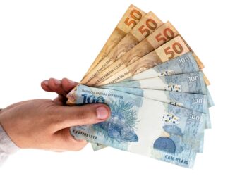 Mão segurando notas de cinquenta e cem reais em leque sobre fundo branco, simbolizando as regras e prazos do Pé-de-Meia Licenciaturas.