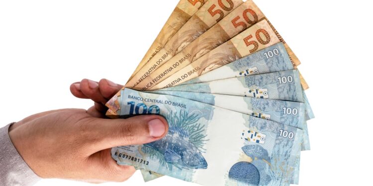Mão segurando notas de cinquenta e cem reais em leque sobre fundo branco, simbolizando as regras e prazos do Pé-de-Meia Licenciaturas.