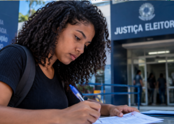 Pessoa preenche documento em frente a unidade da Justiça Eleitoral.