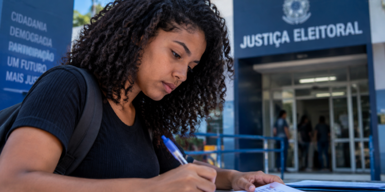 Pessoa preenche documento em frente a unidade da Justiça Eleitoral.