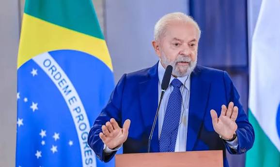 Chefe do Executivo federal discursando em um púlpito com microfone, ao lado da bandeira nacional, durante evento oficial.