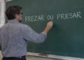 Professor escrevendo as palavras “prezar ou presar” no quadro durante aula de língua portuguesa.