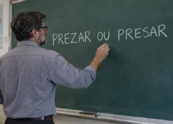 Professor escrevendo as palavras “prezar ou presar” no quadro durante aula de língua portuguesa.