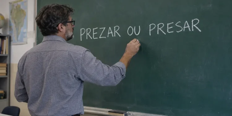 Professor escrevendo as palavras “prezar ou presar” no quadro durante aula de língua portuguesa.